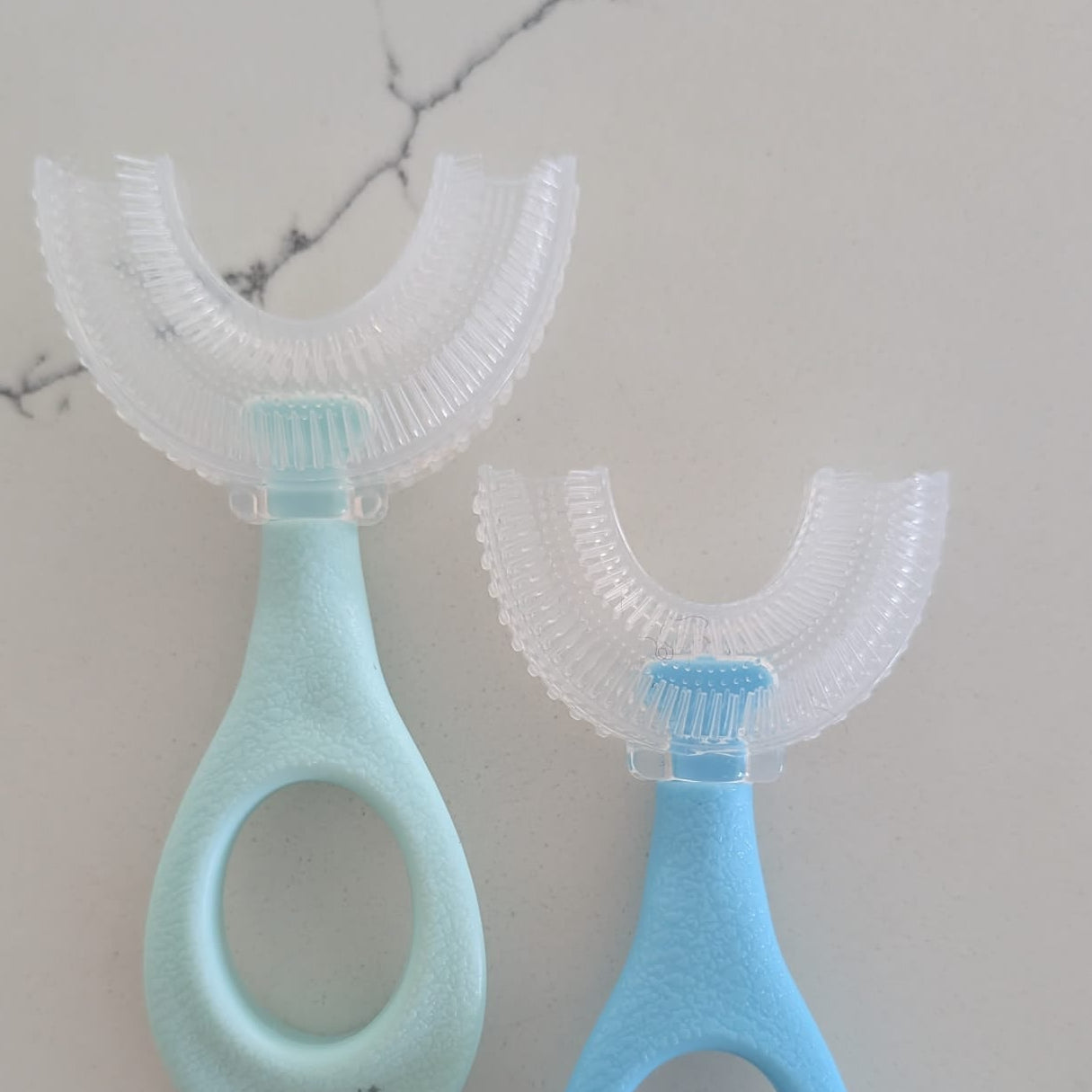 Two baby toothbrushes with soft bristles on a marble surface